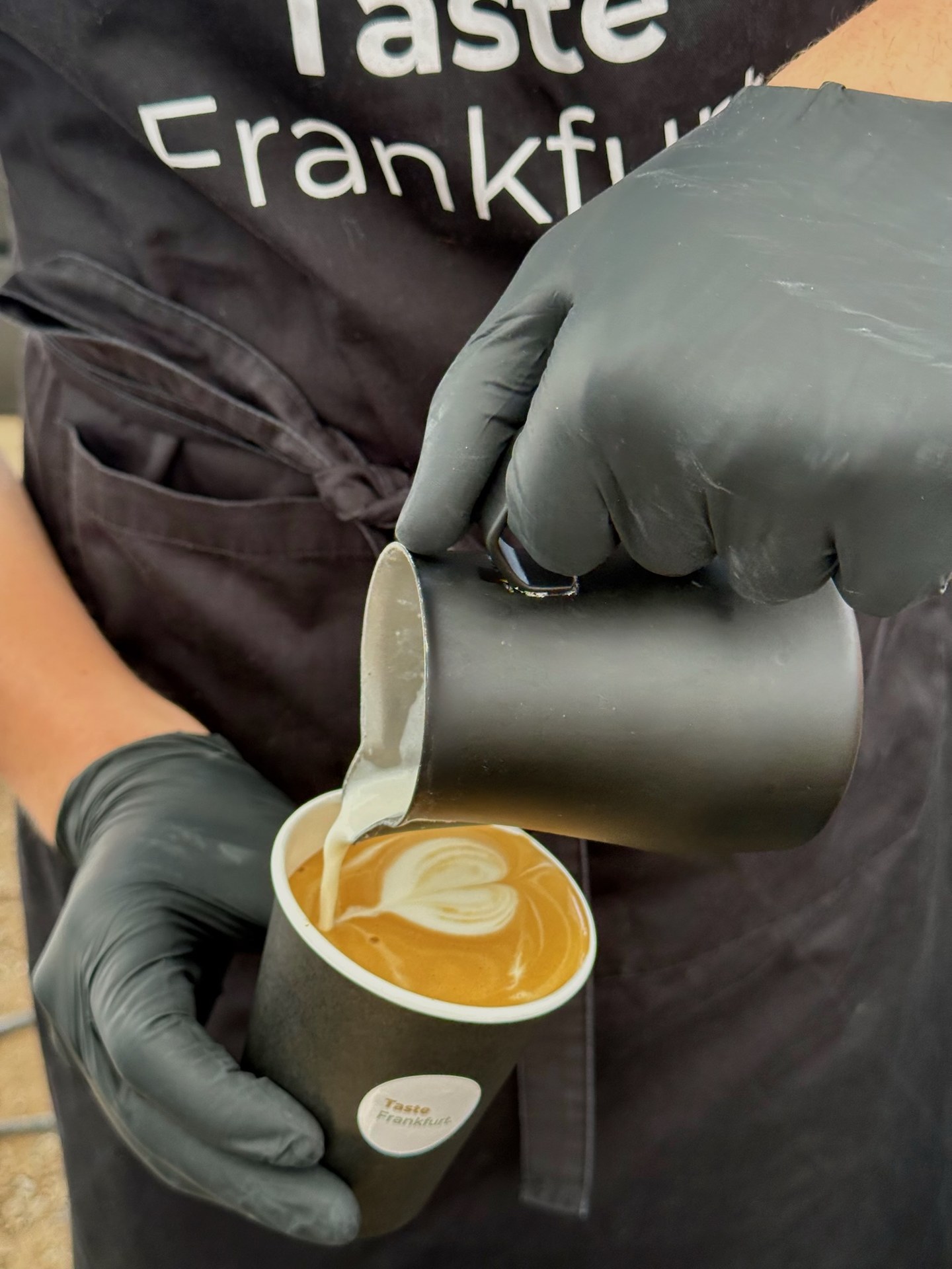 Barista gießt Latte Art Herz in einen Taste Frankfurt Coffee-to-go-Becher